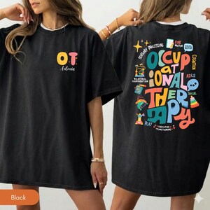 May include: A black t-shirt featuring a small front graphic with the letters OT and the name Antonia. The back displays a large, colorful graphic with the text OCCUPATIONAL THERAPY surrounded by icons and labels like SENSORY PROCESSING.
