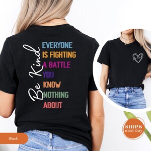 May include: Black t-shirt with the words "Be Kind" in a cursive font on the left side. The back of the shirt has the text "Everyone is fighting a battle you know nothing about" in various colors. A heart design is on the front.