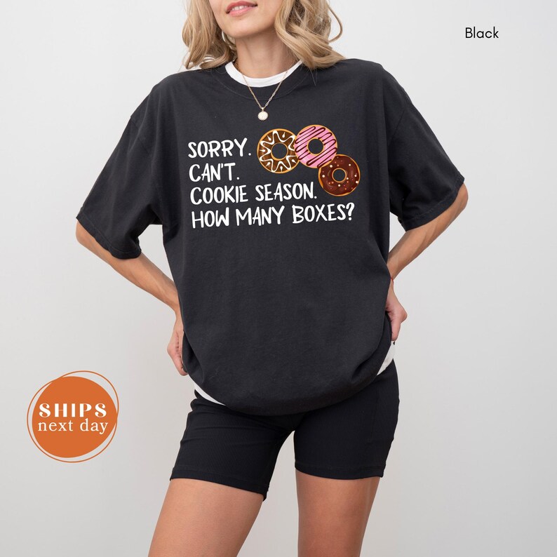 A woman wearing a black t-shirt with a humorous text printed on it, standing against a white background.