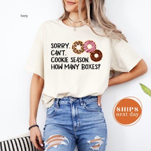 A woman wearing a white t-shirt with a humorous text printed on it, standing against a white background.