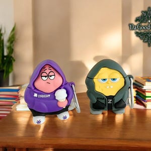 Puede incluir: Dos estuches para AirPod con personajes de dibujos animados. Uno es morado con una cara rosa y el texto "UNBEAT" en la parte delantera. El otro es verde con una cara amarilla y el texto "STYLE" en la parte delantera.