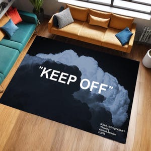 Può includere: Un tappeto rettangolare nero con un design a nuvola e le parole "KEEP OFF" in bianco. Il tappeto presenta un motivo a nuvole blu scuro e bianco. Il tappeto fa parte della collezione IKEA c/o Virgil Abloh "Flooring".