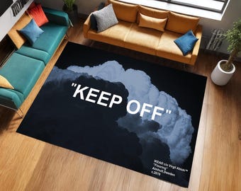 Könnte beinhalten: Ein rechteckiger schwarzer Teppich mit einem Wolkenmuster und den Worten "KEEP OFF" in Weiß. Der Teppich hat ein dunkelblaues und weißes Wolkenmuster. Der Teppich ist Teil der IKEA c/o Virgil Abloh "Flooring" Kollektion.