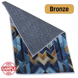 May include: A decorative rug with a geometric pattern in shades of blue, bronze, and white. The rug is labeled "Bronze" and has a "SAMPLE" stamp. The reverse side features a dark gray pattern.