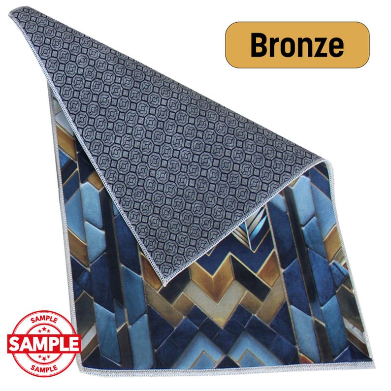 May include: A decorative rug with a geometric pattern in shades of blue, bronze, and white. The rug is labeled "Bronze" and has a "SAMPLE" stamp. The reverse side features a dark gray pattern.