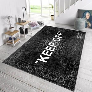 K&ouml;nnte beinhalten: Schwarz-wei&szlig;er gemusterter Teppich mit dem Schriftzug "KEEP OFF" in gro&szlig;en wei&szlig;en Buchstaben. Der Teppich hat ein detailliertes, verziertes Design und liegt auf einem hellen Holzboden.