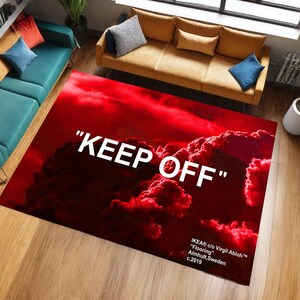 Peut inclure: Tapis rectangulaire rouge avec un motif de nuages et l'inscription blanche "KEEP OFF". Ce tapis fait partie de la collection IKEA c/o Virgil Abloh "Flooring", fabriqué à Almhult, Suède, en 2019.