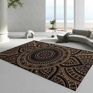 May include: A rectangular area rug with a detailed black and tan mandala design. The rug features a central circular pattern with intricate floral and geometric motifs. The rug is placed on a white floor in a modern living space.