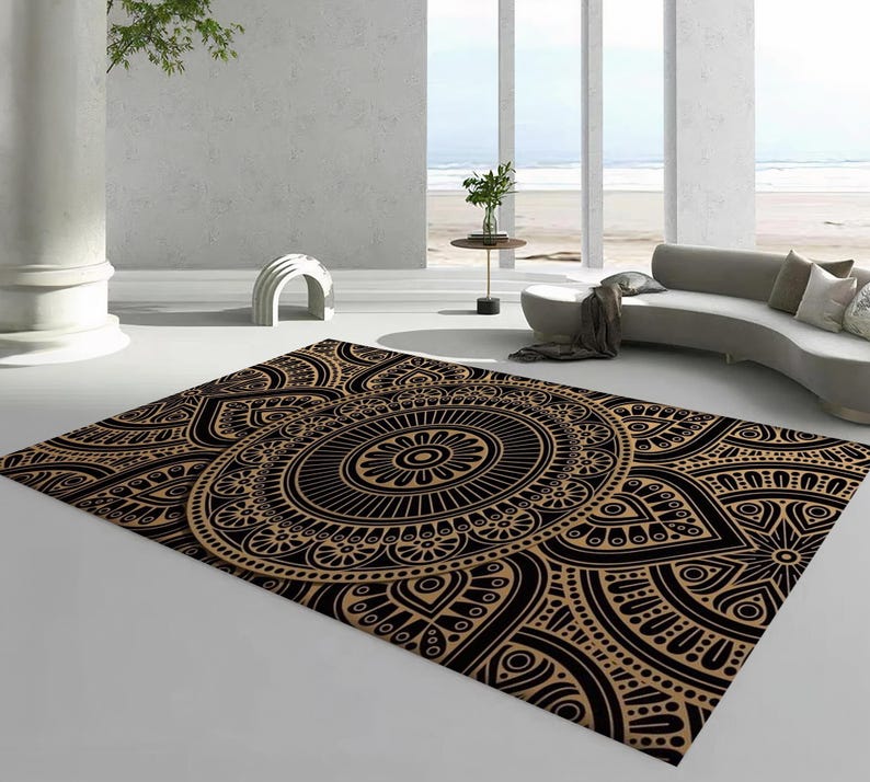 May include: A rectangular area rug with a detailed black and tan mandala design. The rug features a central circular pattern with intricate floral and geometric motifs. The rug is placed on a white floor in a modern living space.