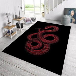 May include: A rectangular black rug featuring a red snake design. The snake is coiled and detailed, with its tongue extended. The rug is placed on a light-colored wooden floor, creating a contrast.
