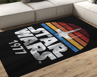 May include: Black rectangular area rug featuring the text "STAR WARS 1977" in white, with a retro-style graphic of a spaceship and a sunset design in red, orange, yellow, and blue.