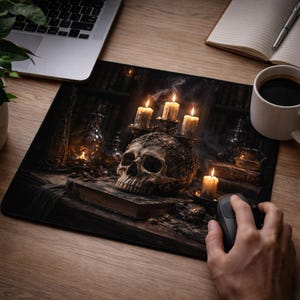 May include: A black mouse mat with a gothic design, showcasing a skull, candles, and books. The skull is central, with lit candles and old books around it. A computer mouse is being used on the mouse mat.
