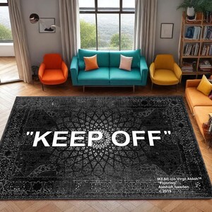 K&ouml;nnte beinhalten: Ein schwarz-grauer Teppich mit Muster und dem wei&szlig;en Schriftzug "KEEP OFF". Der Raum zeigt ein t&uuml;rkisfarbenes Sofa, orangefarbene und gelbe St&uuml;hle und einen Holzboden. Der Teppich misst 240 cm x 300 cm.
