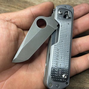 May include: A silver Leatherman Free T4 multi-tool with a partially open blade. The tool has a textured surface and the words "LEATHERMAN FREE T4" are printed on the side.
