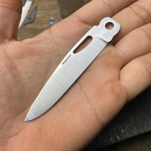 May include: A silver knife blade with a hole in the handle. The blade is marked with the text "MagnaCut".