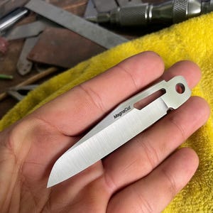 May include: A silver pocket knife with a MagnaCut inscription on the blade. The knife has a small hole near the handle.