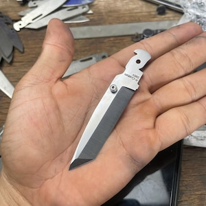 May include: A small, silver pocket knife with a black blade. The knife has a small hole in the handle and the text "K-CUSTOM 580V" is engraved on the handle.