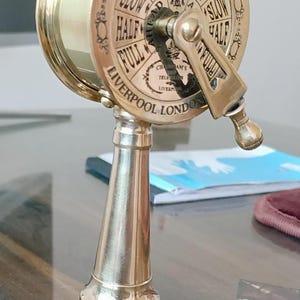 Può includere: Un telegrafo da nave in ottone con una base in legno. Il telegrafo ha un quadrante con le parole "Slow", "Half", "Full", "Stop" e "Stand By". Il quadrante ha anche le parole "Full Speed With Engines" e "Slow Half". Il telegrafo è etichettato "Ship Telegraph" e "Liverpool London".