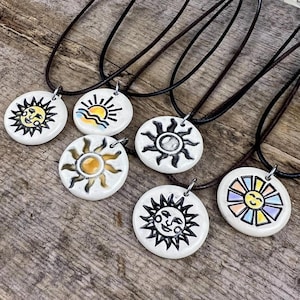 May include: Six ceramic sun pendants on brown leather cords. Each pendant features a different sun design with black outlines and yellow, orange, and blue accents.