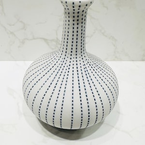 May include: A white ceramic vase with a blue dotted pattern. The vase has a round body and a narrow neck.