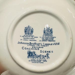 May include: The underside of a white ceramic plate featuring a blue printed maker's mark for Johnson Brothers (Hanley) Ltd, Stoke-on-Trent, England. The text includes Coaching Scenes, Made in England, Dishwasher Safe, and Ironstone.