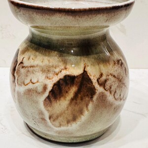 May include: A handcrafted ceramic vase with a unique, organic shape. The vase features a blend of earthy tones, including brown, beige, and green, with a textured, mottled surface. The rim and base are a darker brown, creating a striking contrast.
