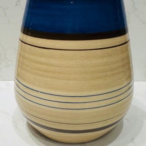May include: A ceramic vase with a blue top and beige body with brown and blue stripes.