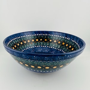 May include: A ceramic bowl featuring a deep blue base colour with a decorative pattern of dark green bands, black circular rings, and small yellow dots. The rim and interior are accented with rows of tiny white dots against a dark blue background.