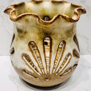 May include: A ceramic vase with a ruffled rim and a cream and brown color scheme. The vase features cut-out designs in a sunburst pattern. The vase is approximately 5 inches tall and 5 inches wide.