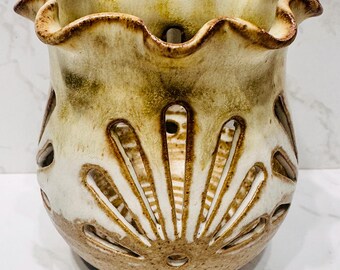 May include: A ceramic vase with a ruffled rim and a cream and brown color scheme. The vase features cut-out designs in a sunburst pattern. The vase is approximately 5 inches tall and 5 inches wide.