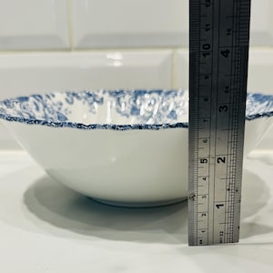 May include: A white ceramic bowl with a blue floral pattern along the scalloped rim. A metal ruler is positioned vertically against the side of the bowl, showing a height of approximately 2.5 inches from the base to the top edge of the rim.