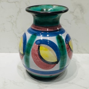 May include: A round ceramic vase with a green, blue, red, and yellow geometric pattern. The vase has a narrow neck and a wide base.