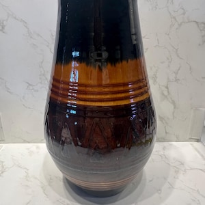 Può includere: Un vaso in ceramica fatto a mano con finitura lucida. Il vaso presenta una sfumatura di colori, che passa da una base marrone scuro a una sezione centrale marrone più chiara e una parte superiore nera. Il vaso ha un design strutturato ed è adatto all'arredamento della casa.