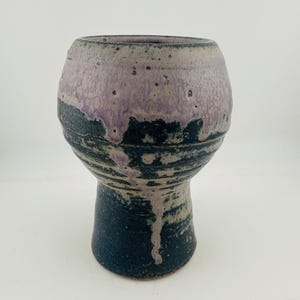 May include: A ceramic vase with a bulbous upper section and a narrower base. The surface features a mottled lavender glaze at the top that drips down over a dark navy blue glaze, creating a textured, layered appearance with visible speckles.