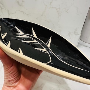 Puede incluir: Un plato de servir de cerámica negro y blanco con un diseño de hoja estilizado. El plato tiene forma ovalada y un acabado brillante.