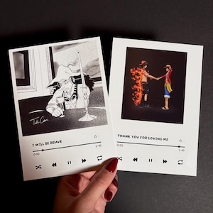 Könnte beinhalten: Zwei Schwarzweißillustrationen von Anime-Charakteren mit Musikplayer-Steuerelementen unter jedem Bild. Das erste Bild zeigt einen Charakter mit Hut und Kerze. Das zweite Bild zeigt zwei Charaktere, wobei ein Charakter von Flammen umhüllt ist. Der Text unter dem ersten Bild lautet "I will be brave" und der Text unter dem zweiten Bild lautet "Thank you for loving me".