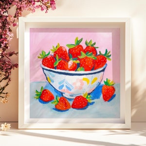 Könnte beinhalten: Eine weiße Keramikschüssel gefüllt mit roten Erdbeeren auf einer hellblauen Oberfläche mit rosa Hintergrund. Die Schüssel hat ein blaues und weißes Blumenmuster.