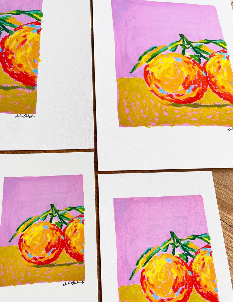 May include: Four prints of a painting depicting two oranges with green leaves on a pink background. The oranges are painted in a stylised way with yellow, orange, and red hues. The background is a light pink colour. The prints are signed "Lilibet".