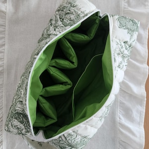 May include: A quilted toiletry bag with a white background and a green pastoral design. The interior is bright green with multiple compartments. The bag has a white zipper and a matching handle. The bag is open, revealing the interior.