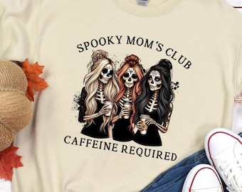 May include: A beige sweatshirt with the text "Spooky Mom's Club Caffeine Required" and a graphic of three skeleton women holding coffee cups.