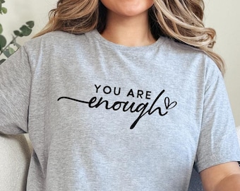 May include: A gray t-shirt with the text "You are enough" in black script with a small heart symbol.