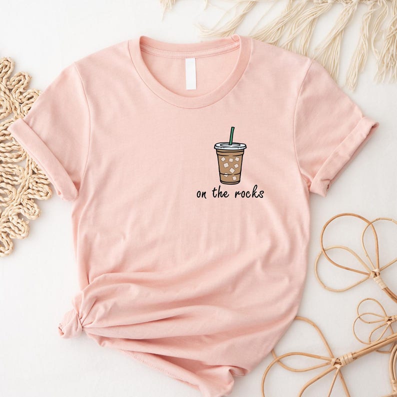 May include: A pink t-shirt with a graphic of a coffee drink with ice and a straw. The text "on the rocks" is below the graphic.