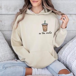 May include: A beige hoodie with a graphic of a coffee cup with ice and a straw. The text "on the rocks" is printed below the cup.