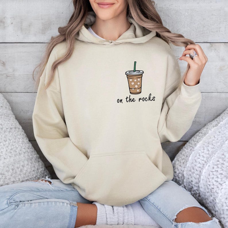 May include: A beige hoodie with a graphic of a coffee cup with ice and a straw. The text "on the rocks" is printed below the cup.