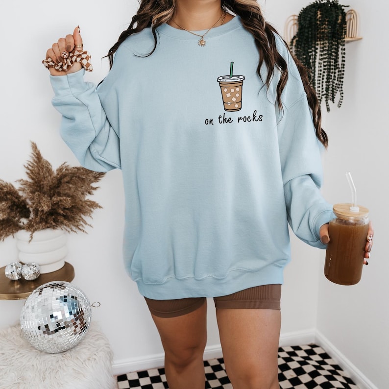 May include: Light blue sweatshirt with a graphic of a coffee cup with ice and the text "on the rocks".