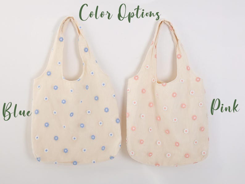 K&ouml;nnte beinhalten: Zwei Tragetaschen mit Blumenstickerei. Die Tasche links hat blaue Blumen und die Tasche rechts hat rosa Blumen. Der Text "Color Options" befindet sich oben im Bild. Der Text "Blue" befindet sich links und der Text "Pink" befindet sich rechts.