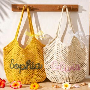 Puede incluir: Dos bolsos de ganchillo con patrones de punto abierto. El bolso amarillo lleva el nombre Sophia en cursiva verde oscuro, y el bolso crema lleva el nombre Olivia en rosa claro. Cada bolso est&aacute; adornado con un lazo de cinta transparente a juego.