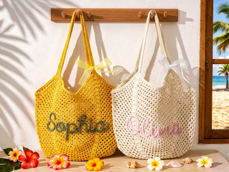 Puede incluir: Dos bolsos de ganchillo con patrones de punto abierto. El bolso amarillo lleva el nombre Sophia en cursiva verde oscuro, y el bolso crema lleva el nombre Olivia en rosa claro. Cada bolso est&aacute; adornado con un lazo de cinta transparente a juego.