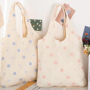 K&ouml;nnte beinhalten: Zwei Einkaufstaschen mit Blumenmustern. Die Tasche links hat blaue Blumen und die Tasche rechts hat rosa Blumen.
