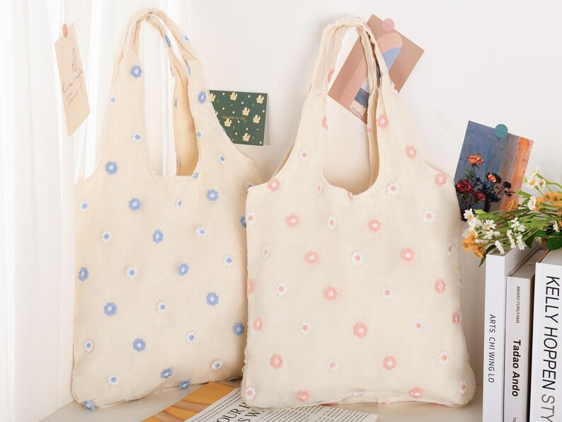 K&ouml;nnte beinhalten: Zwei Einkaufstaschen mit Blumenmustern. Die Tasche links hat blaue Blumen und die Tasche rechts hat rosa Blumen.